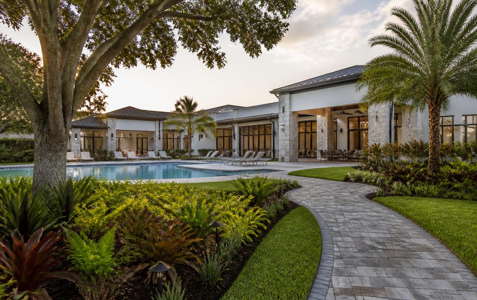 An upscale Florida master-planned community clubhouse and resort pool framed by mature landscaping in late-afternoon light