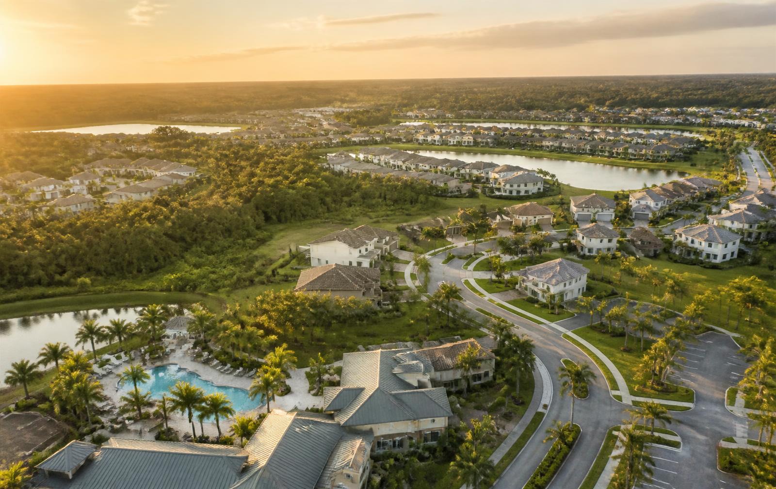 Golden-hour aerial of a Wesley Chapel master-planned community showing lakes, palm-lined streets, distinct neighborhood sections and a pool amenity center